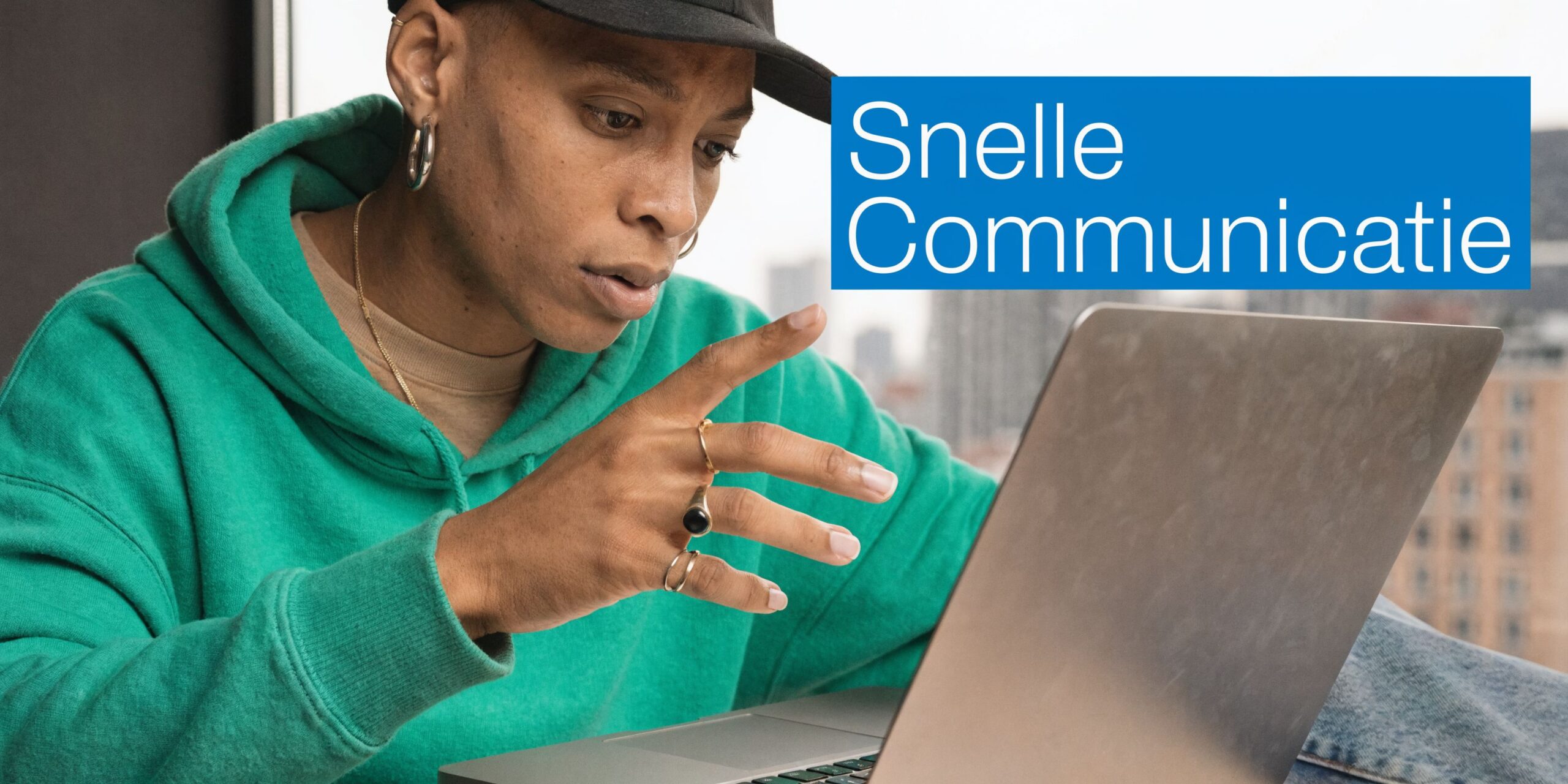 Een jongeman in een groene hoodie gebruikt een laptop voor snelle communicatie in een modern kantoor.